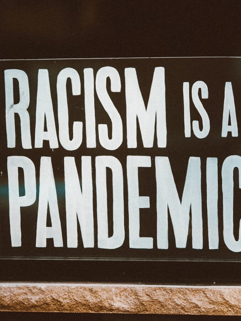 Sign with bold white text on a black background reads, "RACISM IS A PANDEMIC.