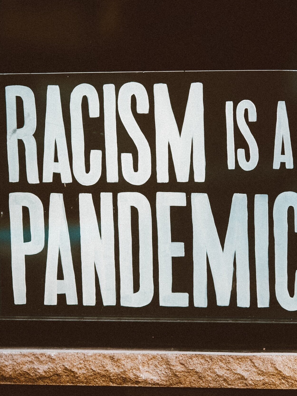 Sign with bold white text on a black background reads, "RACISM IS A PANDEMIC.
