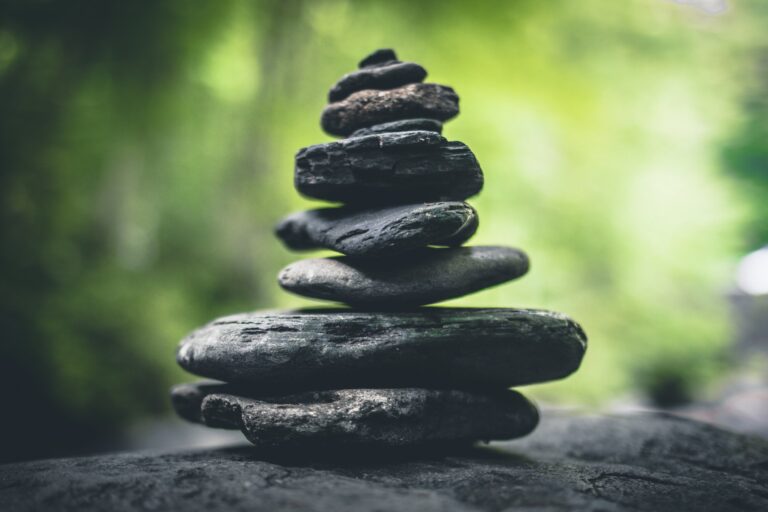 A stack of smooth, dark gray stones balances on top of each other against a blurred green background, creating a calming and natural scene.