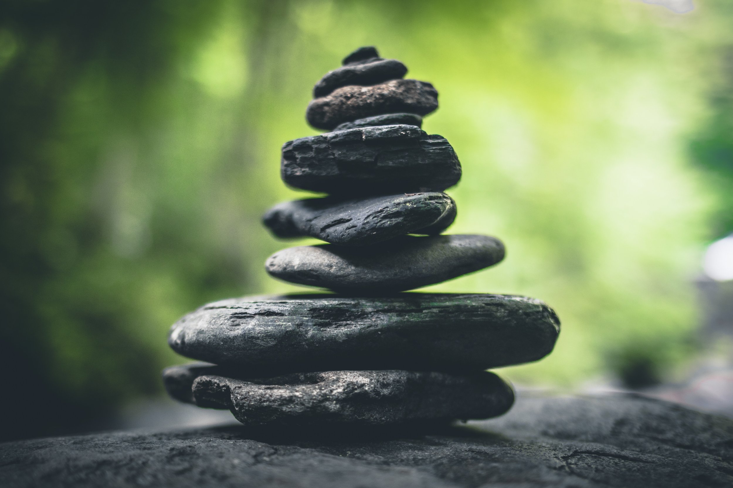 A stack of smooth, dark gray stones balances on top of each other against a blurred green background, creating a calming and natural scene.