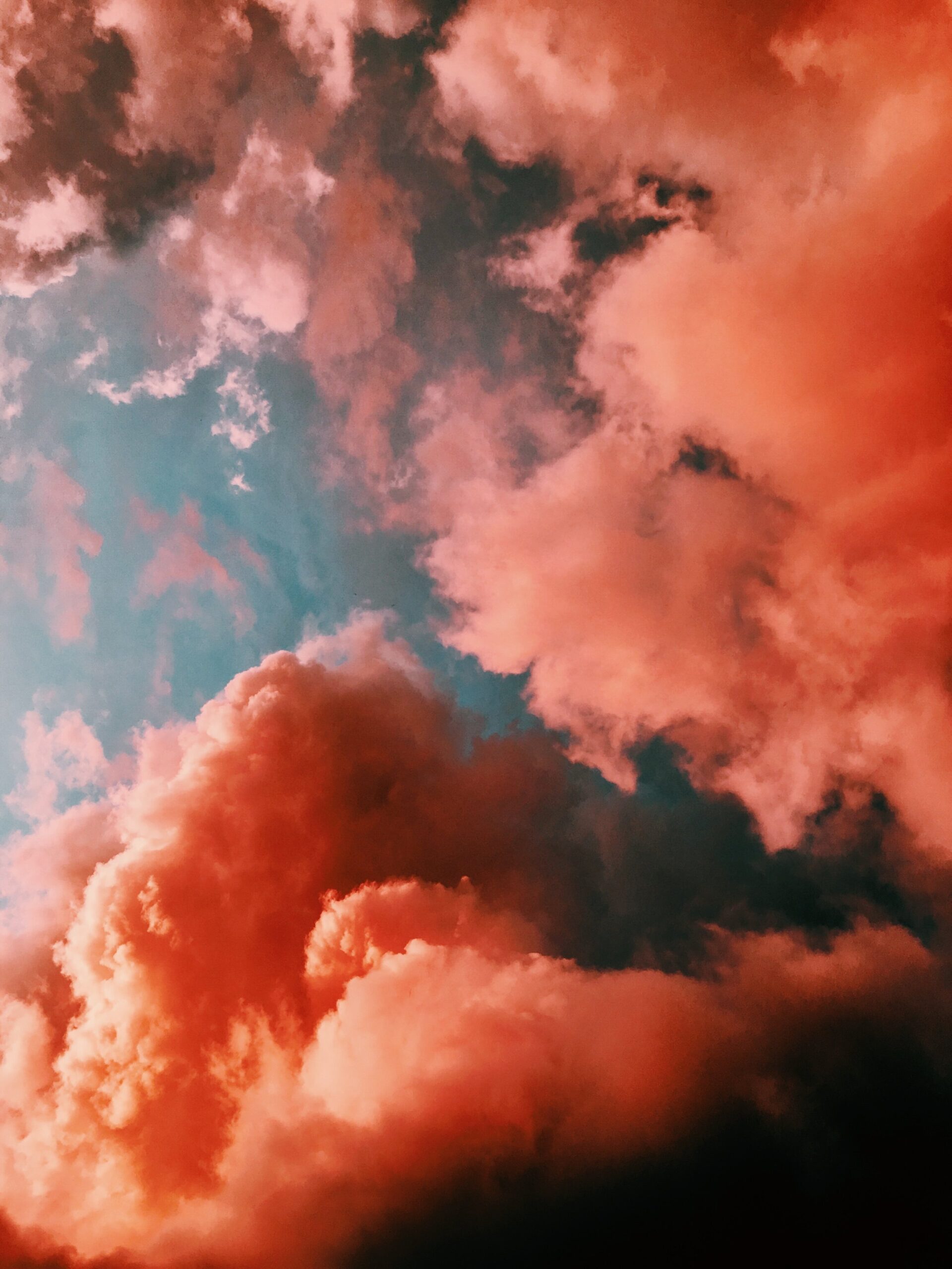 A dramatic sky with large, fluffy clouds illuminated in shades of pink and orange against a backdrop of deep blue. The clouds appear vibrant and textured, creating a striking contrast with the rich blue sky.
