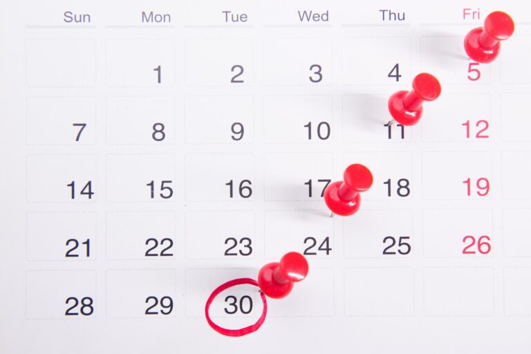 A calendar page displays dates for a month, starting on Sunday. Red pushpins mark Fridays, and the 30th is circled in red.
