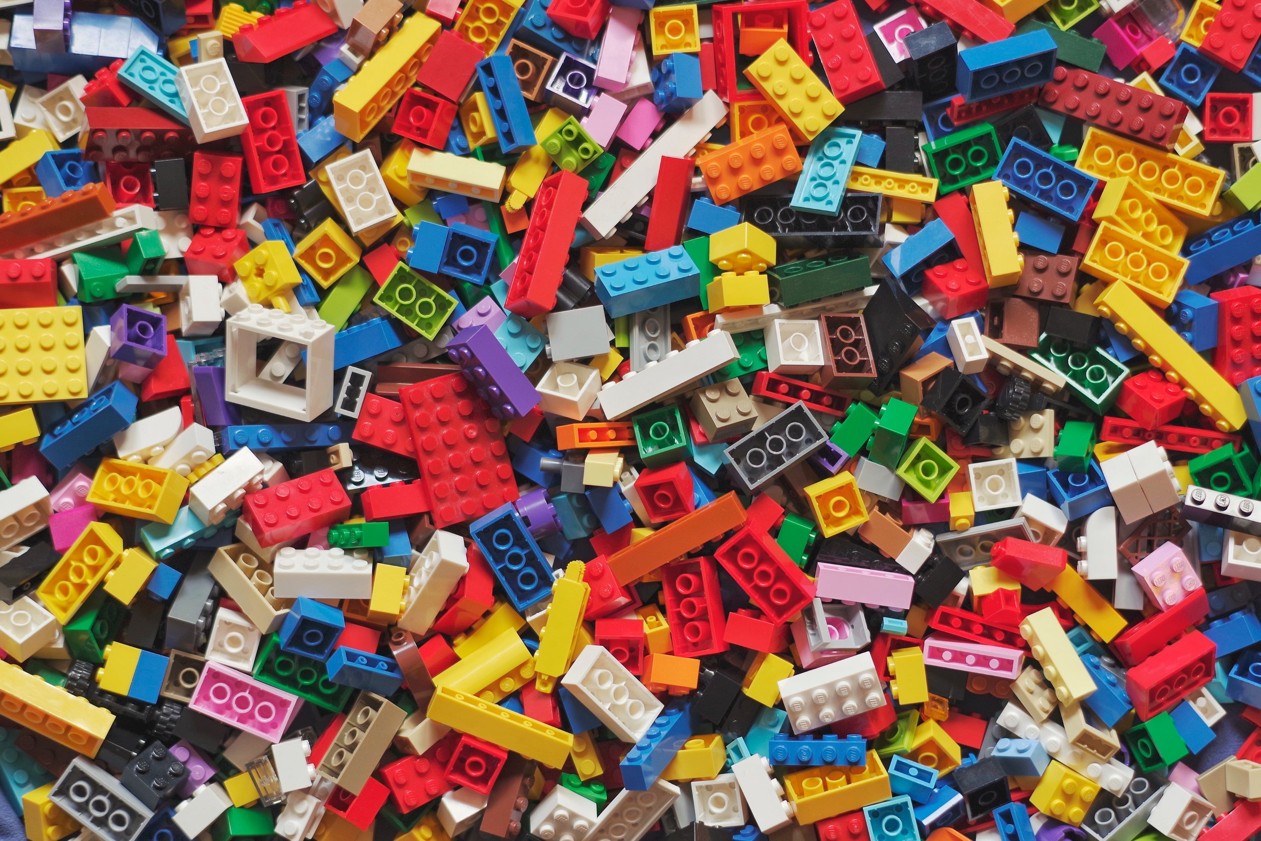 A large pile of colorful LEGO bricks scattered randomly. The bricks are of various shapes and sizes, featuring a wide range of colors including red, blue, yellow, green, black, and white.