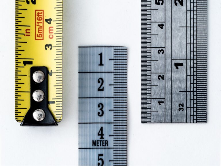 Three measuring tools are displayed vertically against a white background: a yellow tape measure on the left, a clear plastic ruler in the center, and a silver metal ruler on the right.